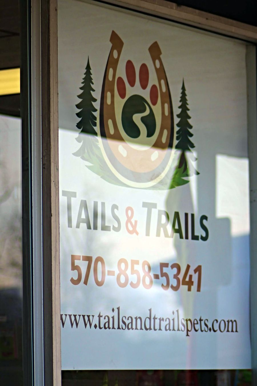 The shop's front window with the Tails & Trails logo, phone number and website
